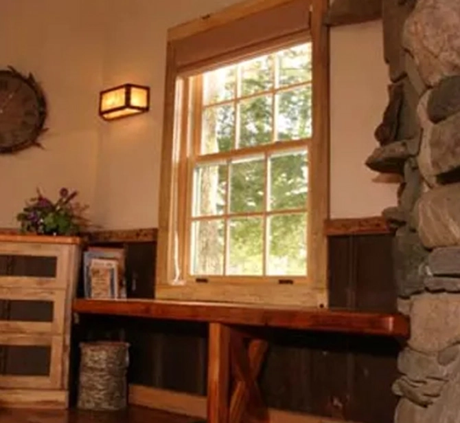 A window in the corner of a room with a table and chair.